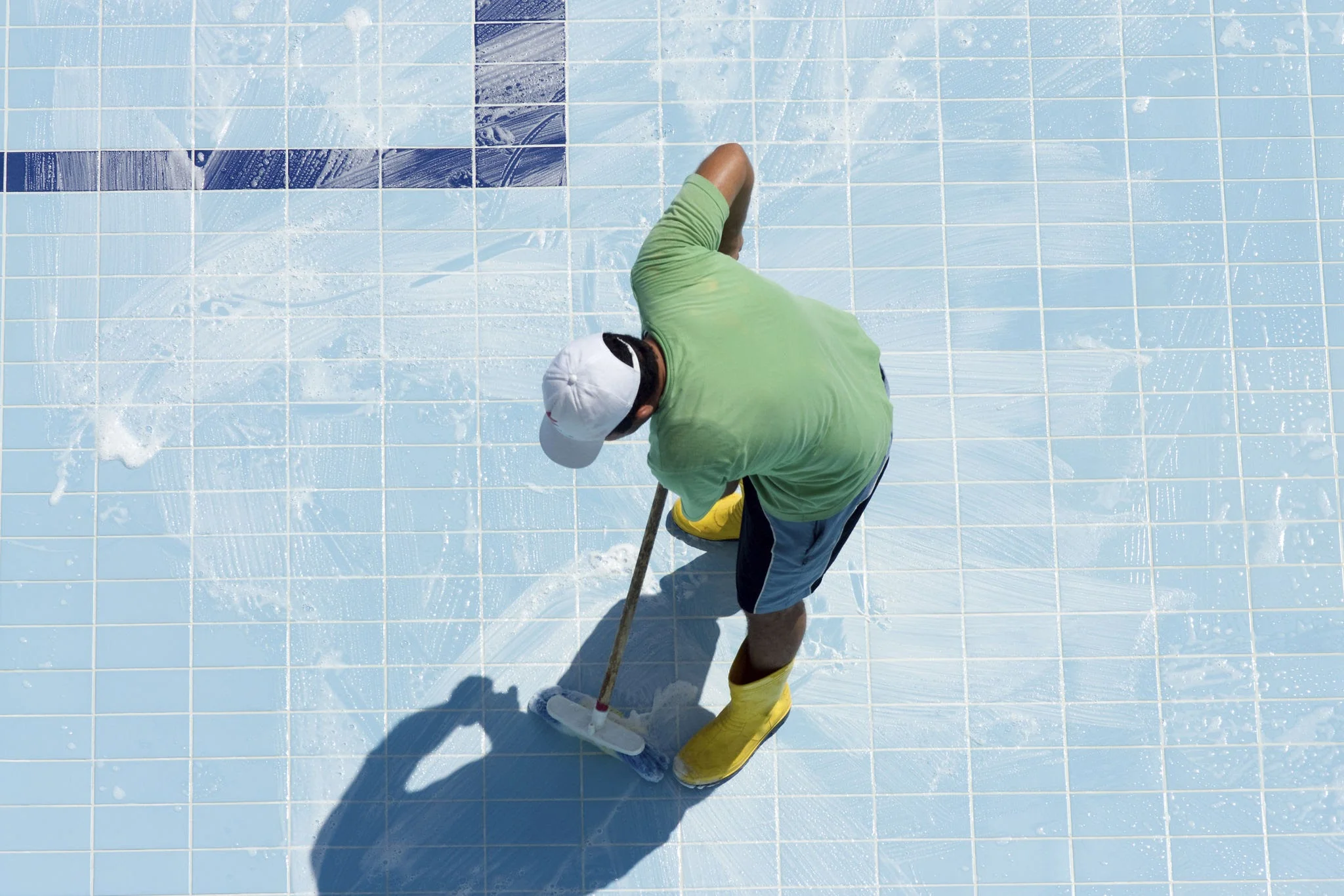 Pool Paint Types Explained: Which One Is Right for Your Sydney Pool? 1 A pool painter in protective gear applying coating to a drained concrete pool with a roller showing professional application technique. Conveys expertise and quality workmanship
